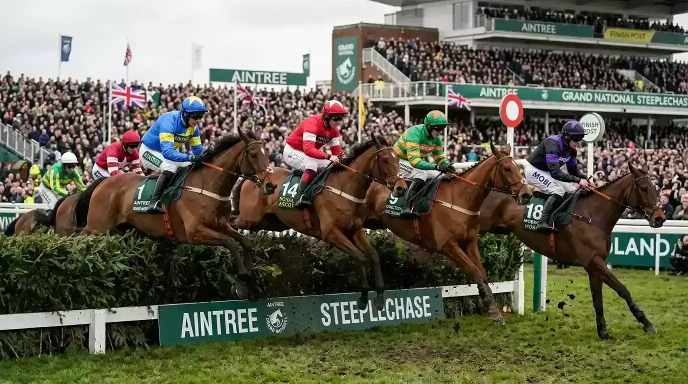 Horses jumping a large brush fence during the Grand National at Aintree racecourse